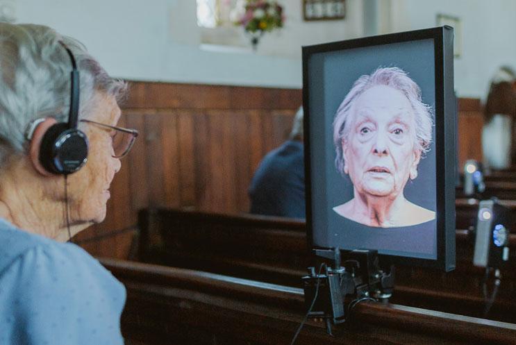 Lady wearing headphones watching a talking head on a portrait digital screen.